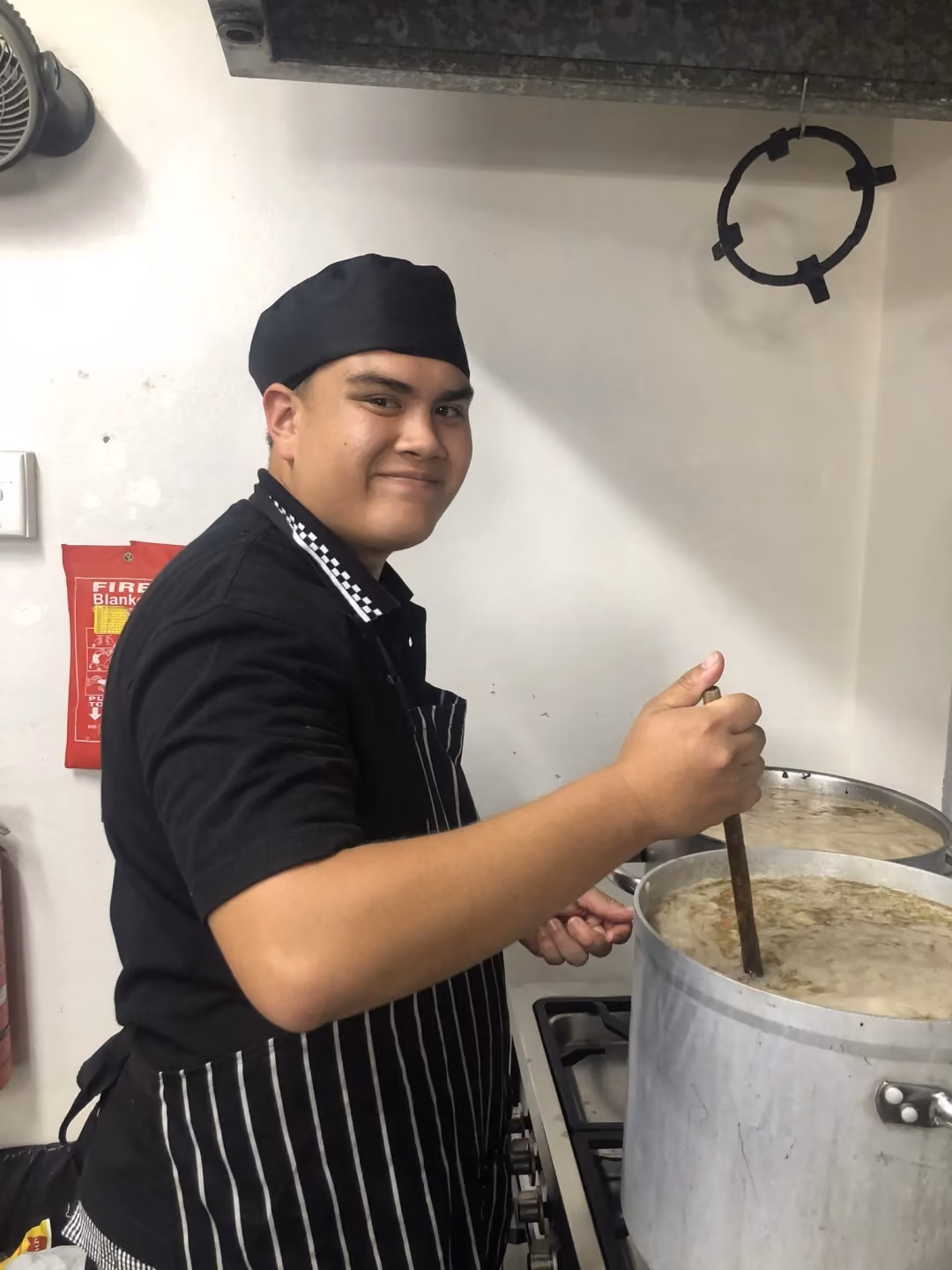 Young trainee cook stirring a large pot in the kitchen
