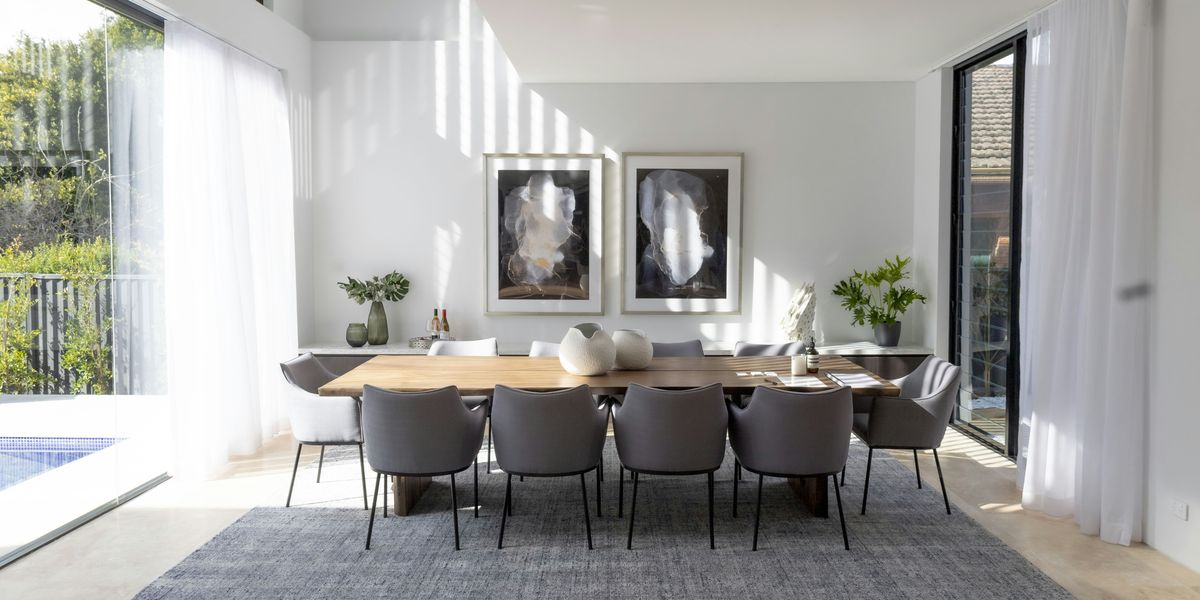 Sunlit dining room with a sculptural wood table, upholstered chairs, and floor-to-ceiling glass overlooking a pool