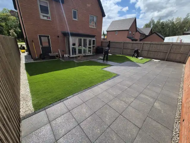 Grey paved patio with rattan table and chairs and artificial lawn in a Manchester garden