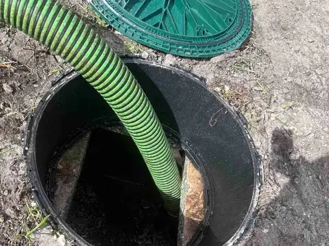 Green vacuum hose lowered into an open septic tank during a pump-out