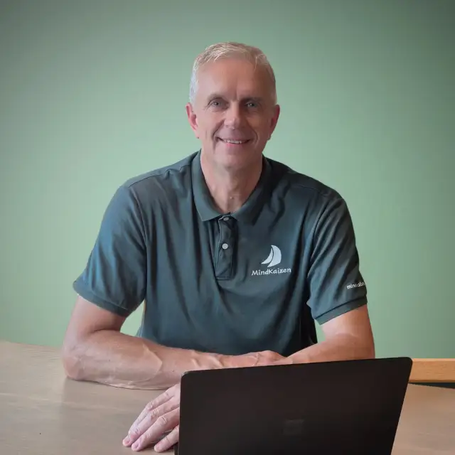 Peter Weiss seated at a desk in a MindKaizen polo shirt.