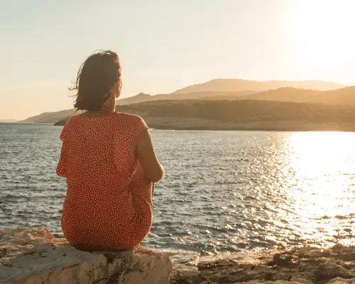 Person sitting thoughtfully near a calm lake at sunset