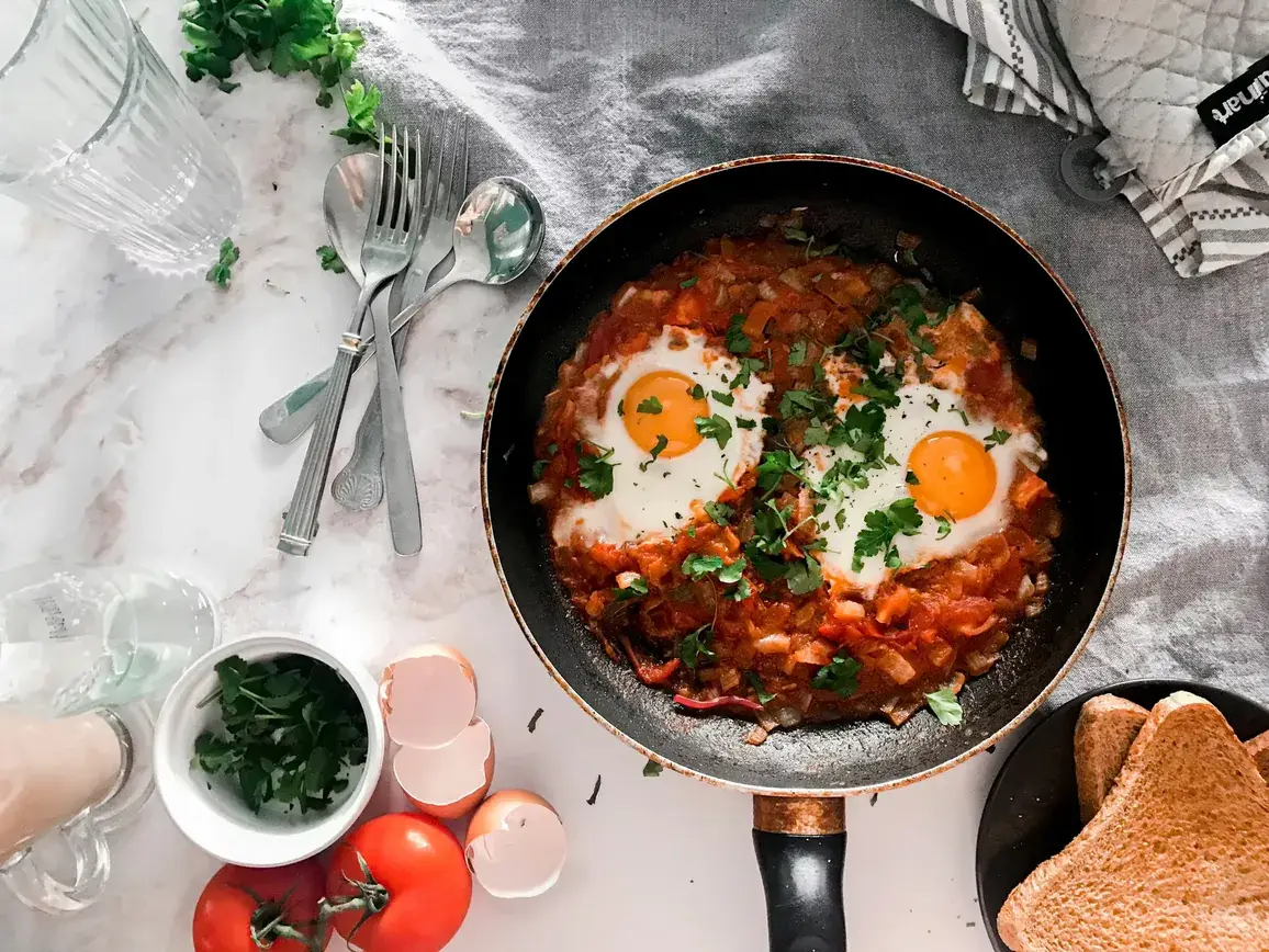 Shakshuka with two eggs in a frying pan, topped with parsley and served with wholegrain toast