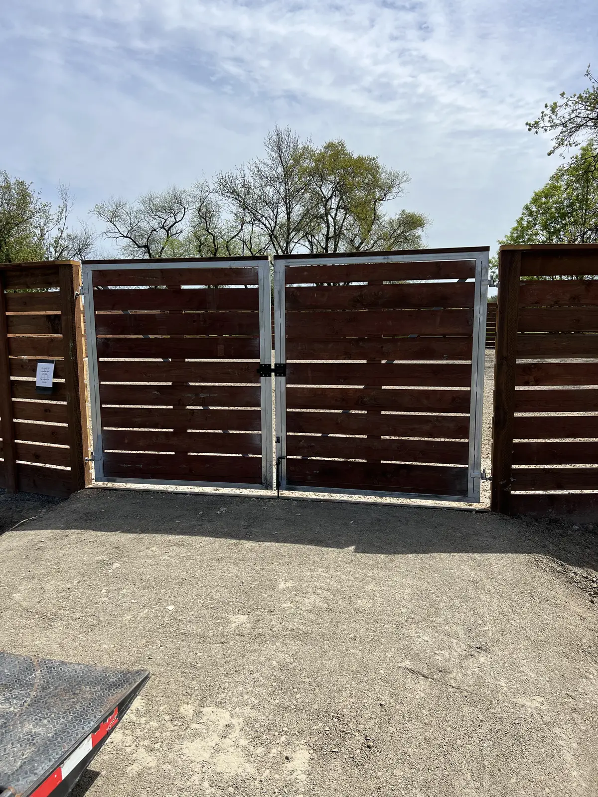 Double driveway gate with galvanized steel frames and horizontal stained redwood infill, set in a matching horizontal board fence
