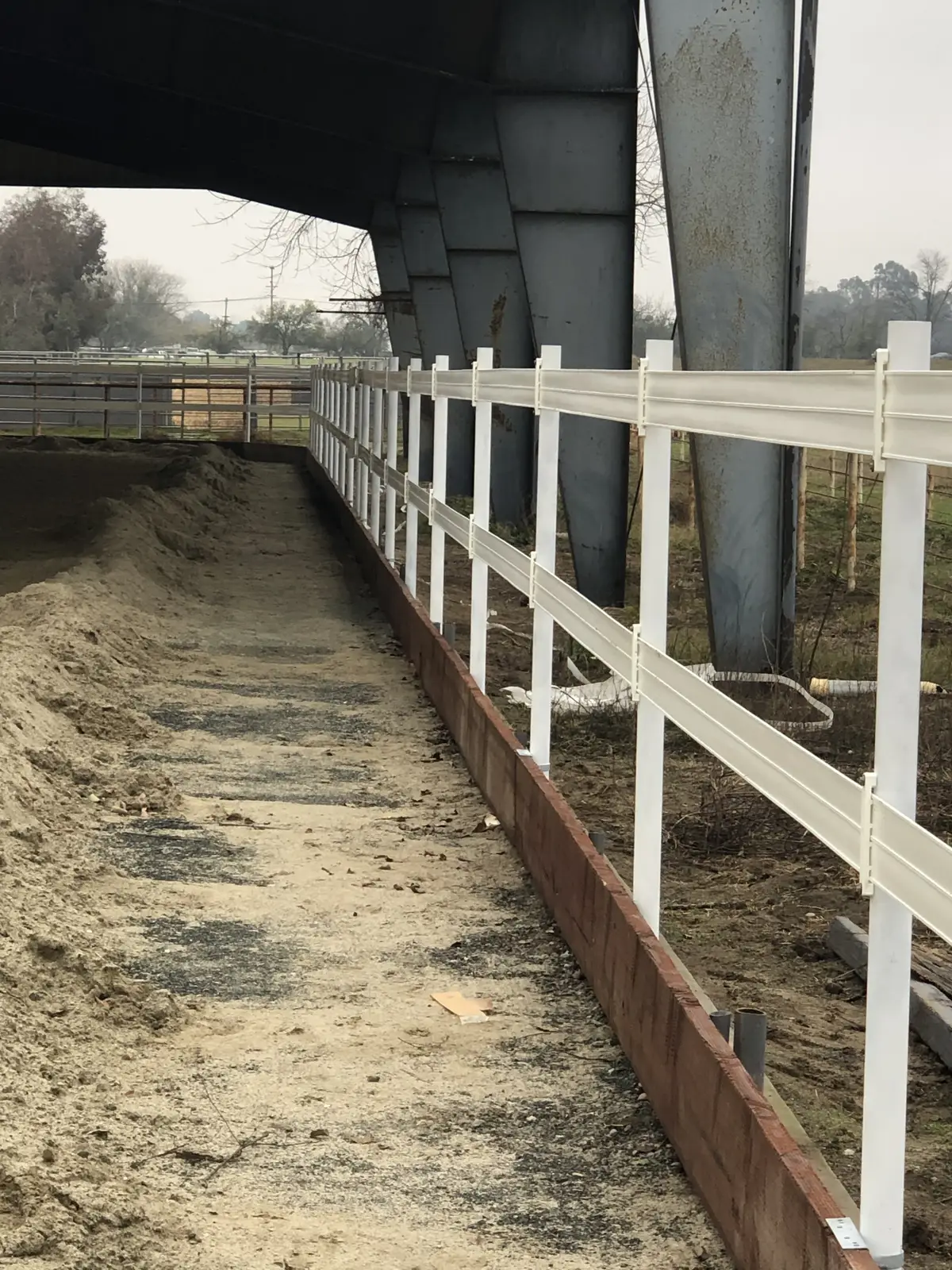 White three-rail vinyl fence on a wood kickboard inside a covered riding arena