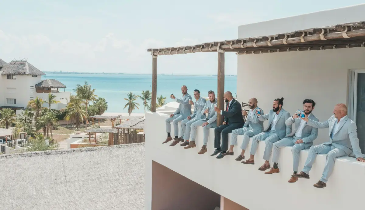 A destination wedding with the Groomsmen in light blue suits and the Groom in a dark suit sitting on a railing.