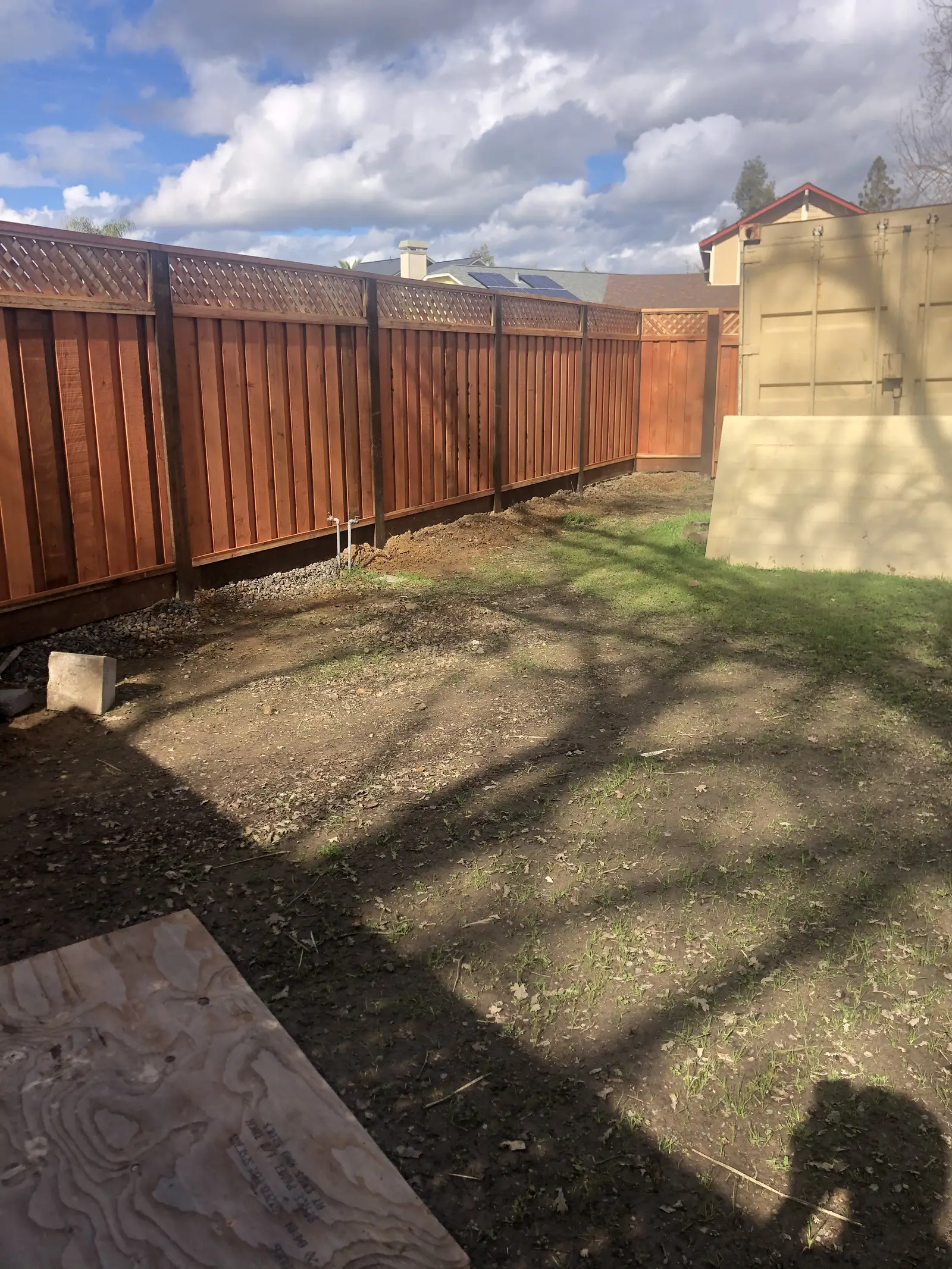 Long lattice-top redwood privacy fence along a backyard with a shed, under puffy clouds
