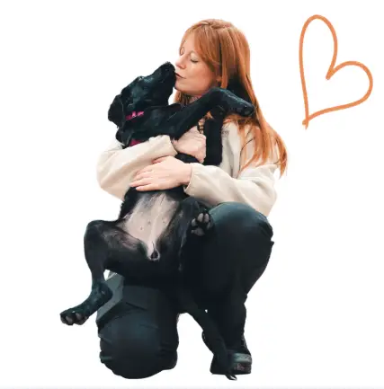 Leanne hugging a black dog with a heart