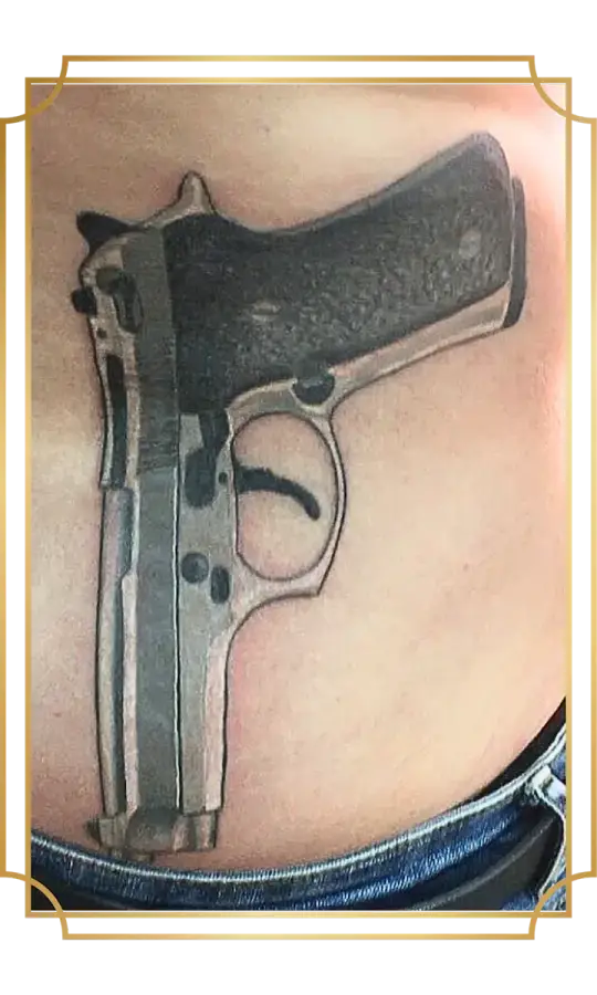 Black-and-gray realism pistol tattoo on the lower abdomen with a textured grip, metallic highlights and detailed mechanical features, created in San Marcos