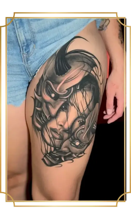 Black and gray woman's face tattoo framed by Japanese armor and mask details on the thigh