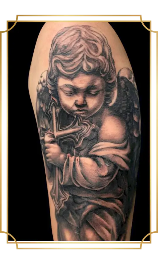Black and gray cherub angel holding a cross tattoo on the arm