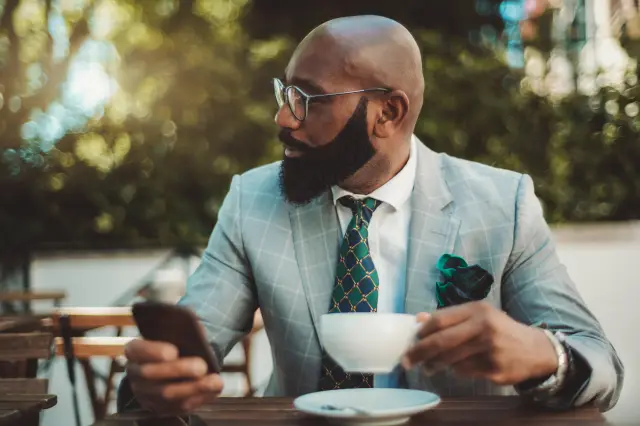 A man with broad shoulders wearing a properly fitted custom made-to-measure suit in light grey windowpane with a deep green tie