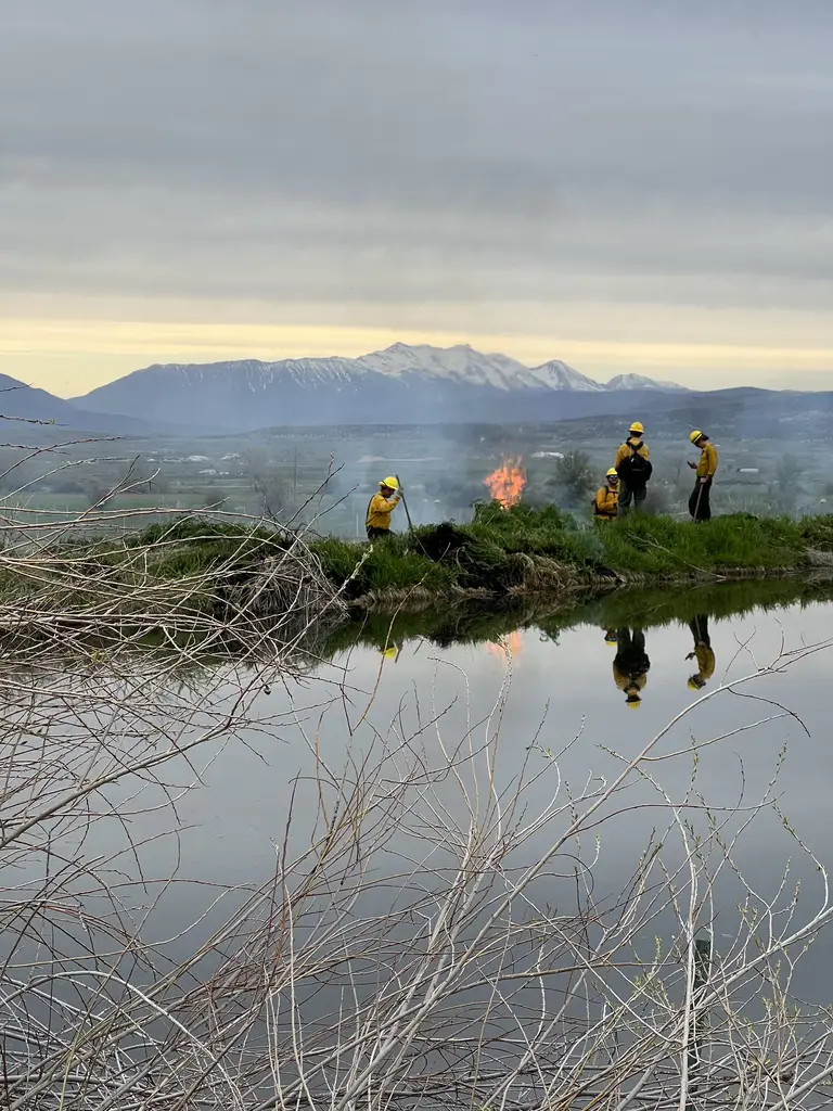 Firefighters working a fire line beside a water channel at dusk, mountains in the distance