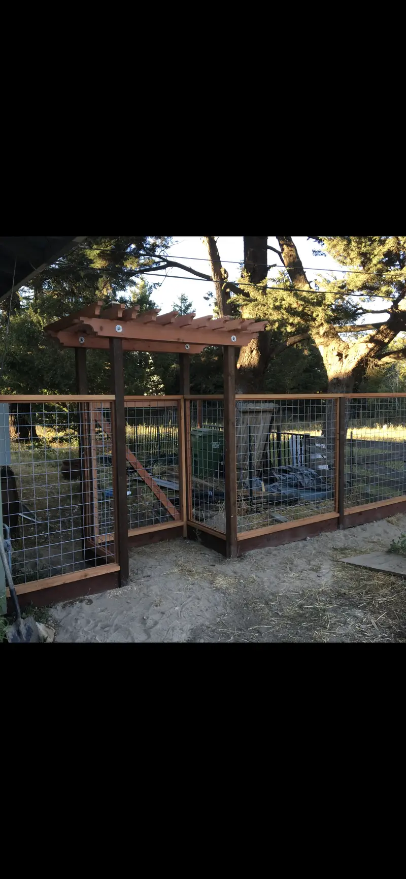 Redwood-framed welded-wire garden enclosure with an arbor over the entry and a diagonal-braced walk gate