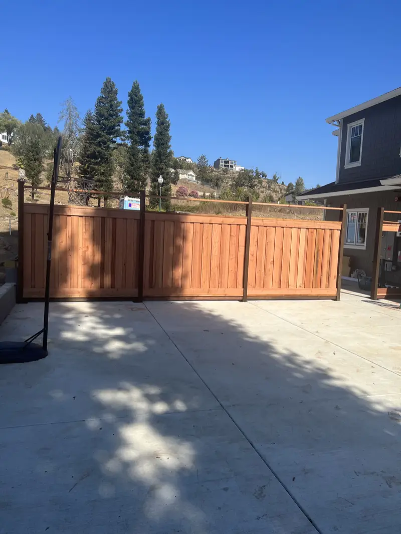 Redwood privacy fence with framed panels enclosing a new concrete backyard pad below hillside homes
