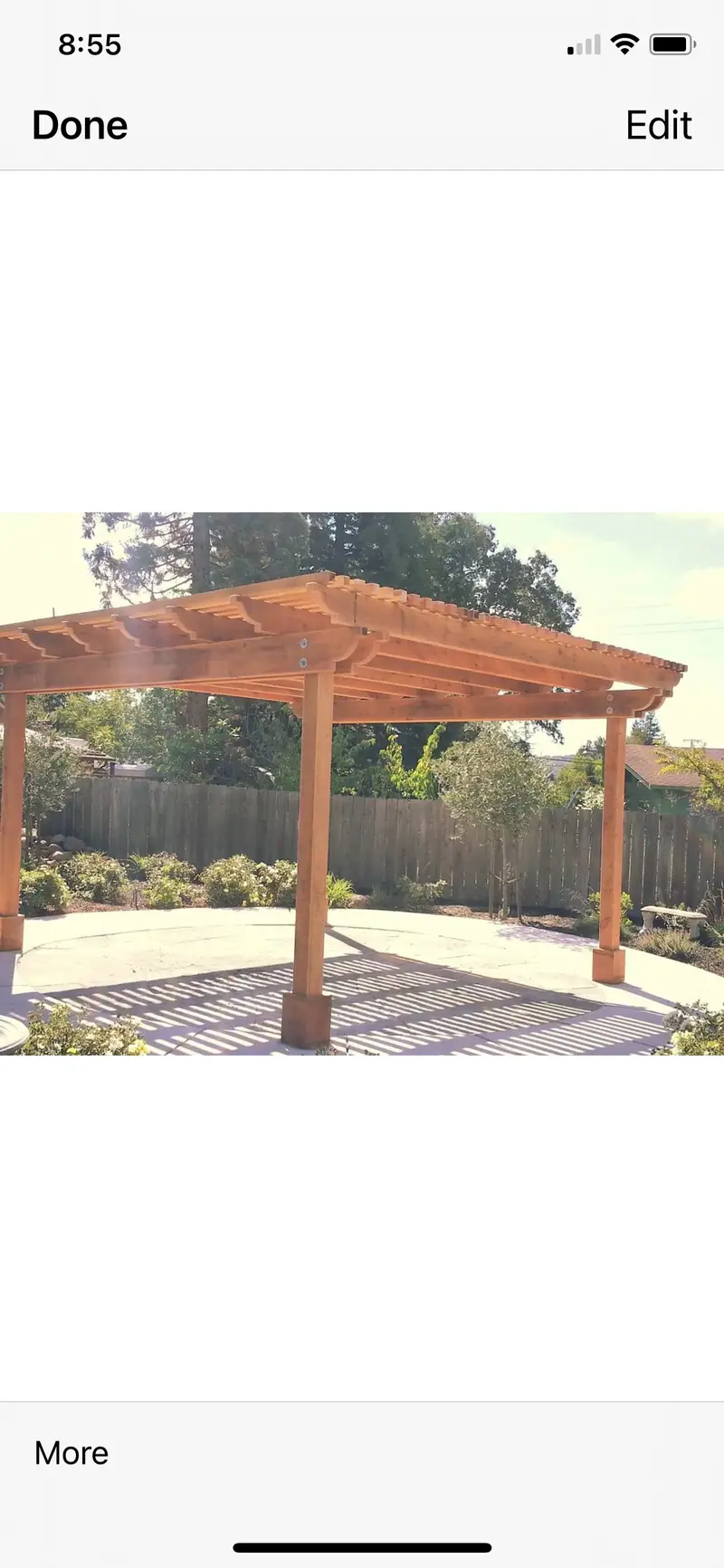 Freestanding redwood pergola with notched rafter tails over a curved concrete patio, wood fence and plantings behind