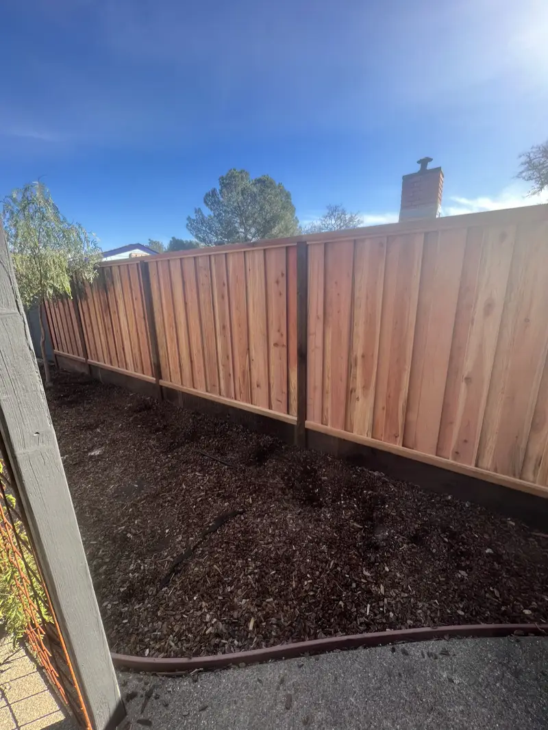 Redwood board-and-batten fence with dark posts and kickboard above a fresh mulch bed
