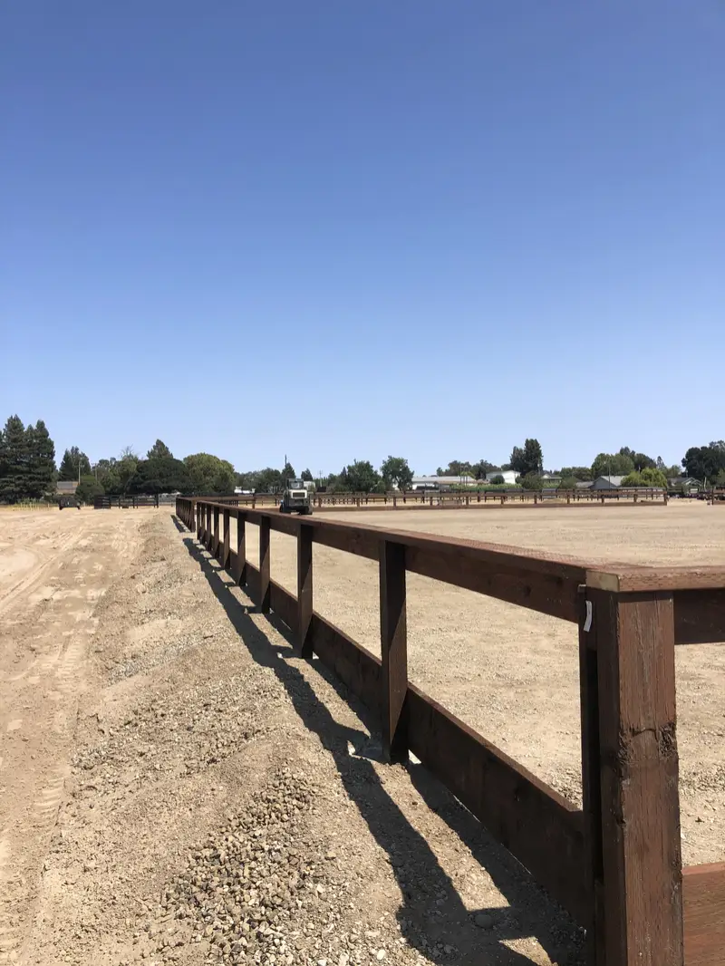 Two-rail stained wood arena fence with a kickboard around a large graded sand arena