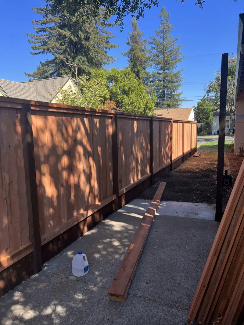 Redwood privacy fence with framed panels and dark posts along a concrete side yard