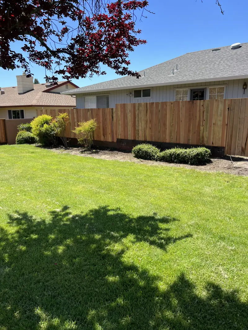 New redwood board fence with kickboard behind a lawn and shrub bed beside a single-story home
