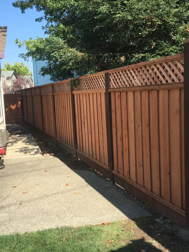 Redwood privacy fence with a lattice top, dark-stained posts and kickboard lining a concrete side-yard walkway, matching wood gate at the far end