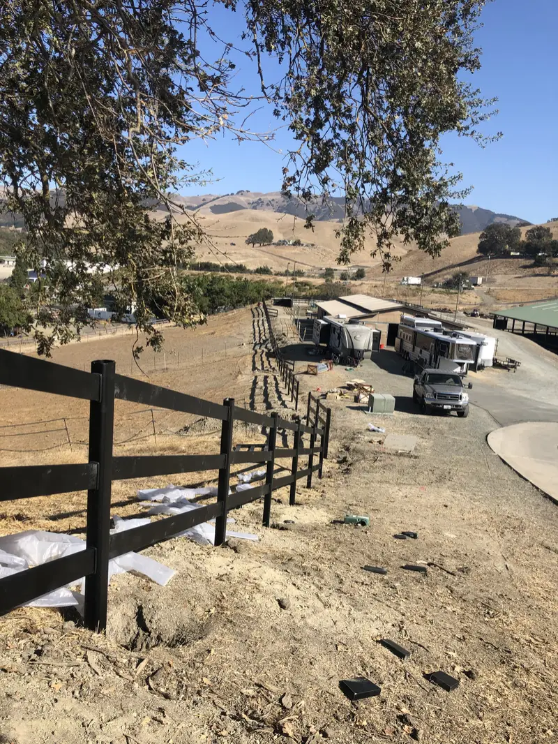 Solid horizontal redwood round pen on open ranch land with valley oaks, pickup truck parked beside it