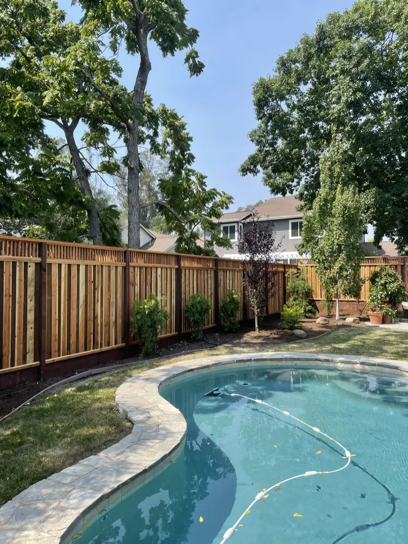 Redwood privacy fence with slatted top and dark posts behind a kidney-shaped pool and new plantings