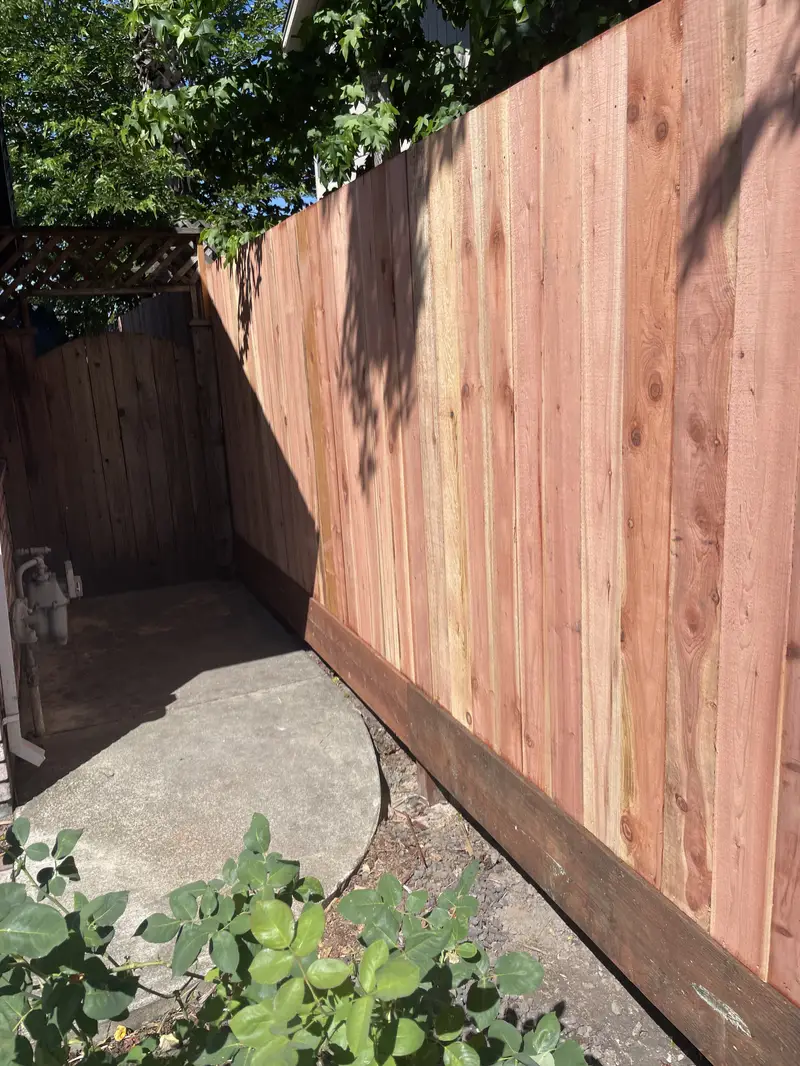 Close-up of new redwood board fence with kickboard beside a concrete pad and an arched wood side gate