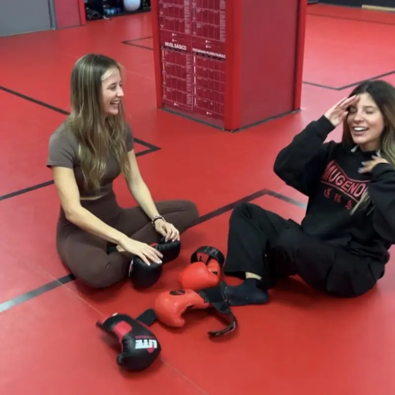 Dos alumnas sentadas en el tatami riendo después del entrenamiento, con los guantes en el suelo