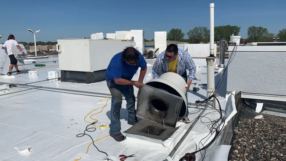 Two Repair King roofers flashing a rooftop exhaust fan on a white PVC roof