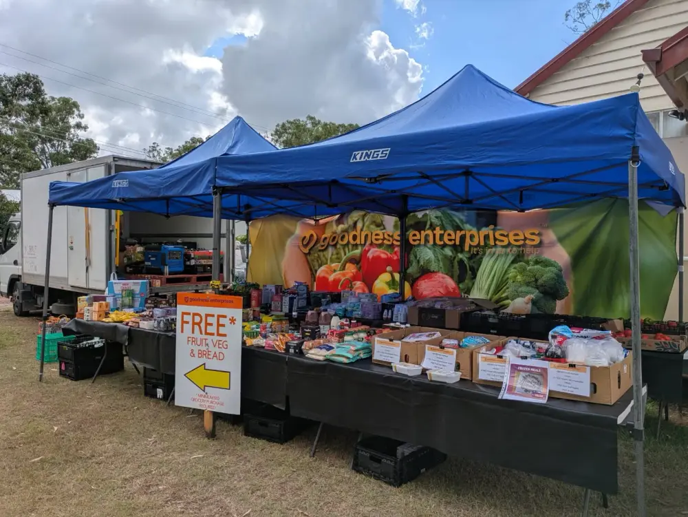 Goodness Enterprises market marquees with a free food sign and a table of groceries