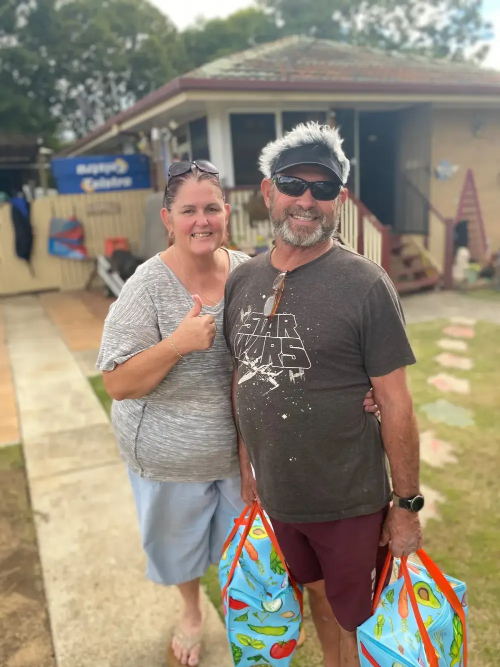 Two locals smiling outside with bags of Goodness groceries