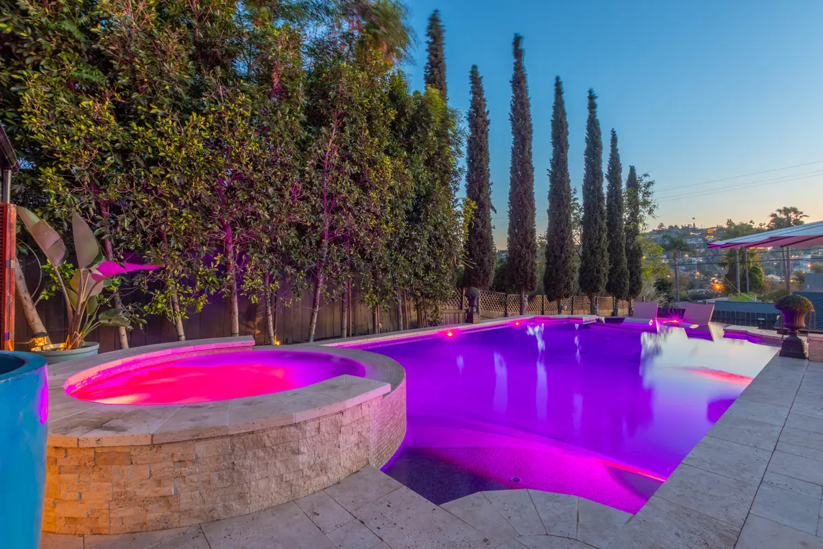 Raised stone spa glowing magenta beside a lit pool at dusk