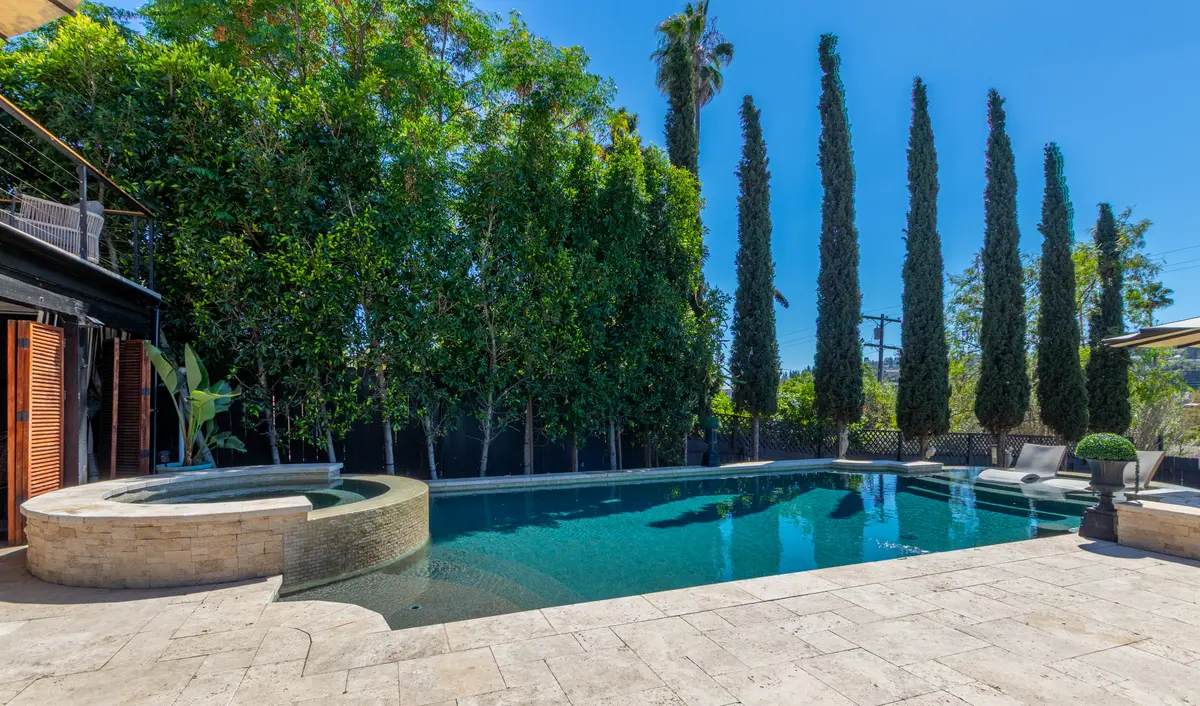 Stacked-stone spa and freeform pool lined with cypress trees