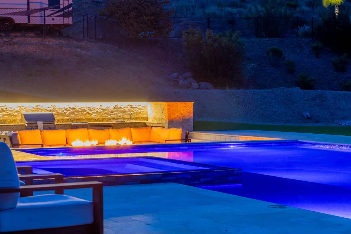 Linear fire wall glowing behind a blue-lit pool at night