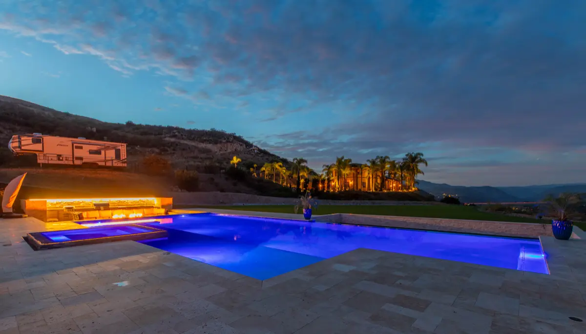 Linear fire wall glowing behind a blue-lit pool at night
