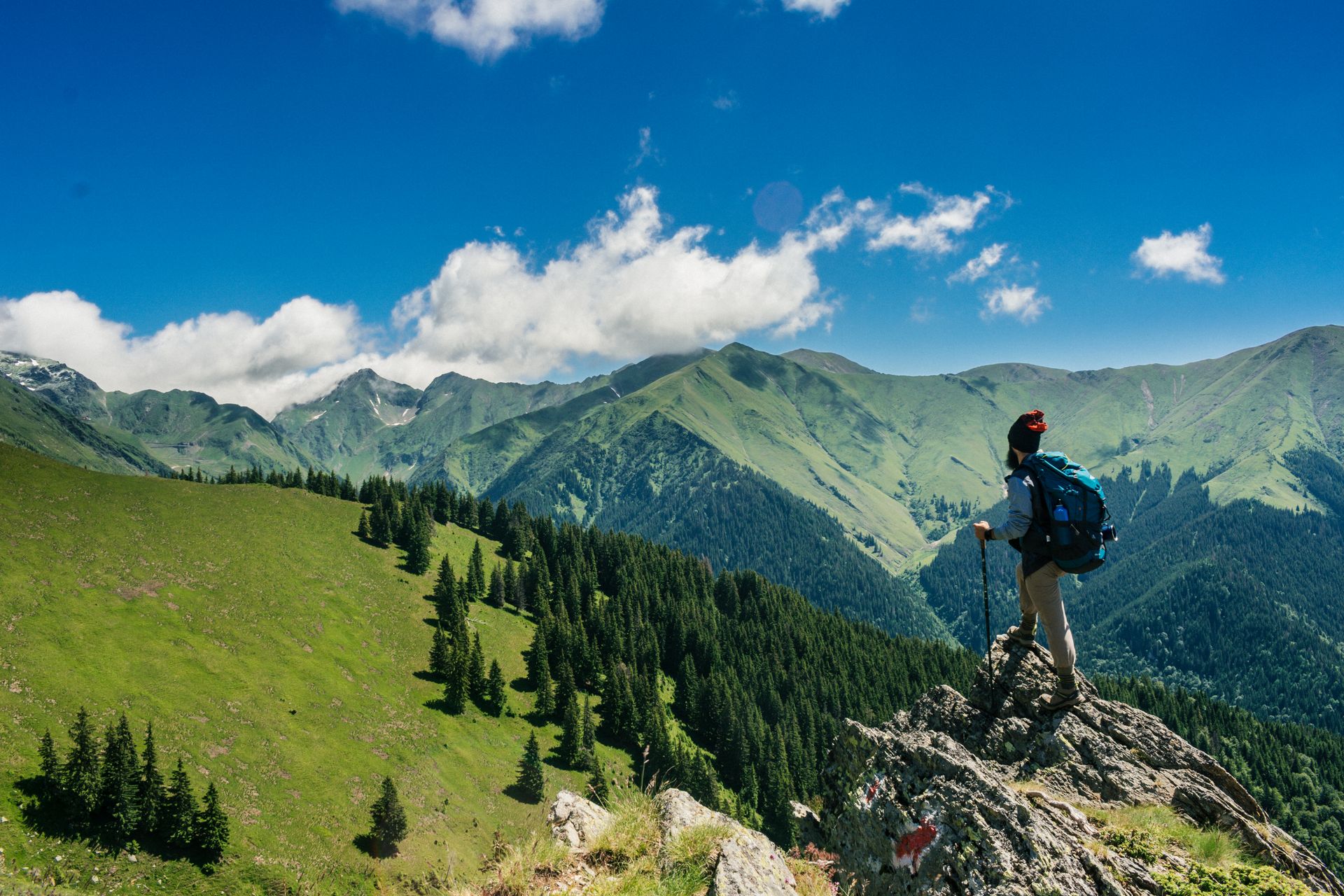 Hiker on a mountain ridge overlooking green peaks
