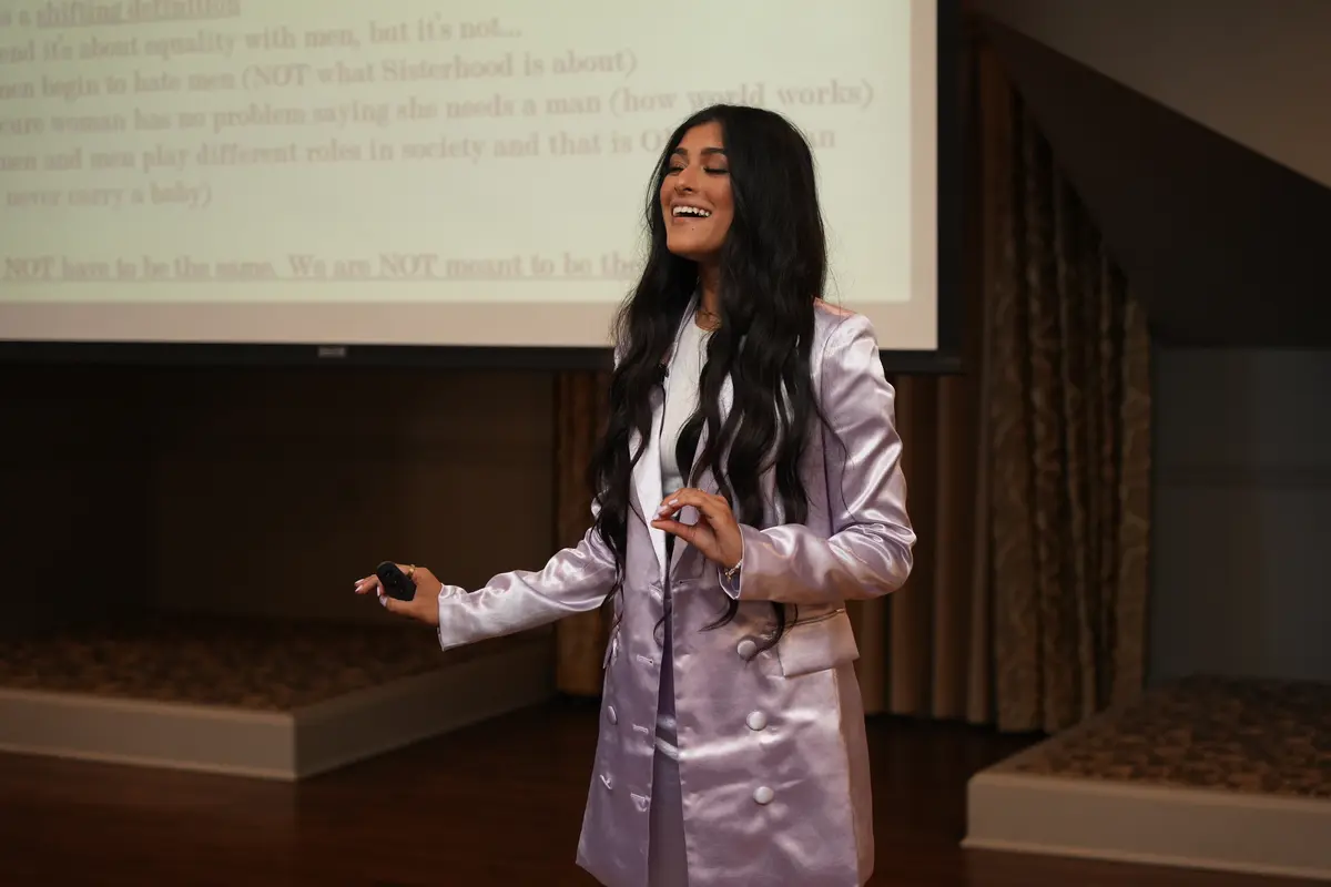 Amber Farooqui smiling during a presentation in a lavender suit