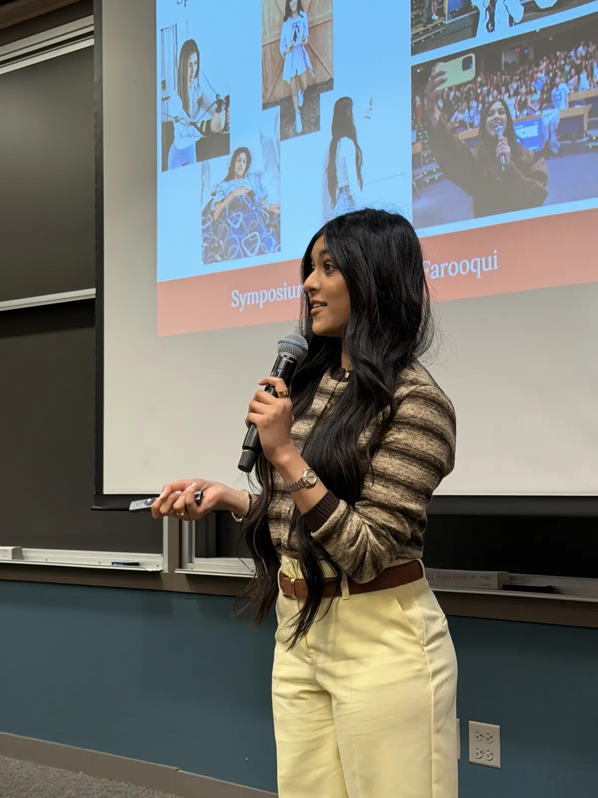 Amber Farooqui presenting with a microphone in a striped top and cream trousers