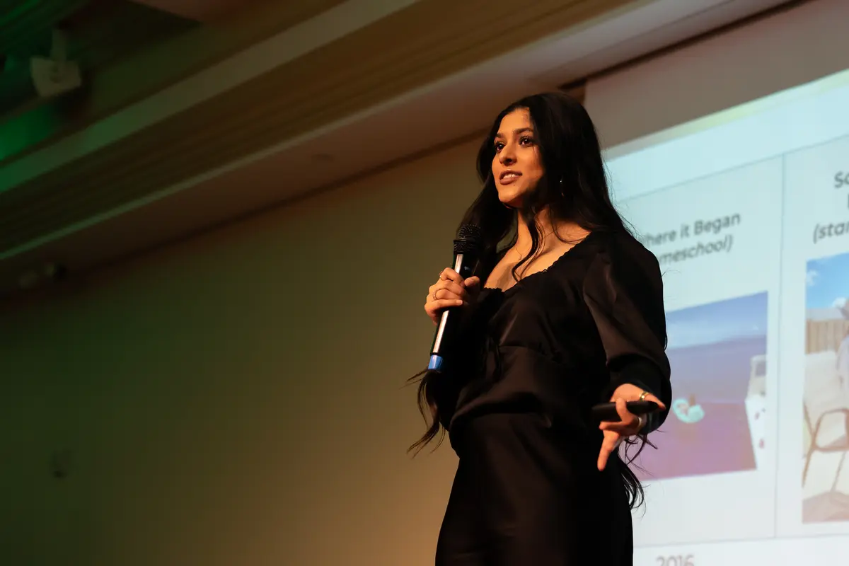 Amber Farooqui speaking on stage in a black outfit