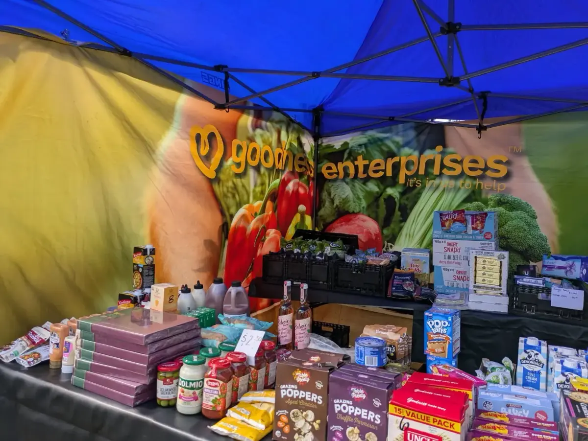 Goodness Enterprises market table stocked with rescued groceries under a blue marquee