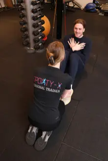 Een coach begeleidt een deelnemer op de trainingsvloer bij Sporty-x