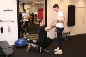 Een coach begeleidt een lid op de trainingsvloer bij Sporty-x
