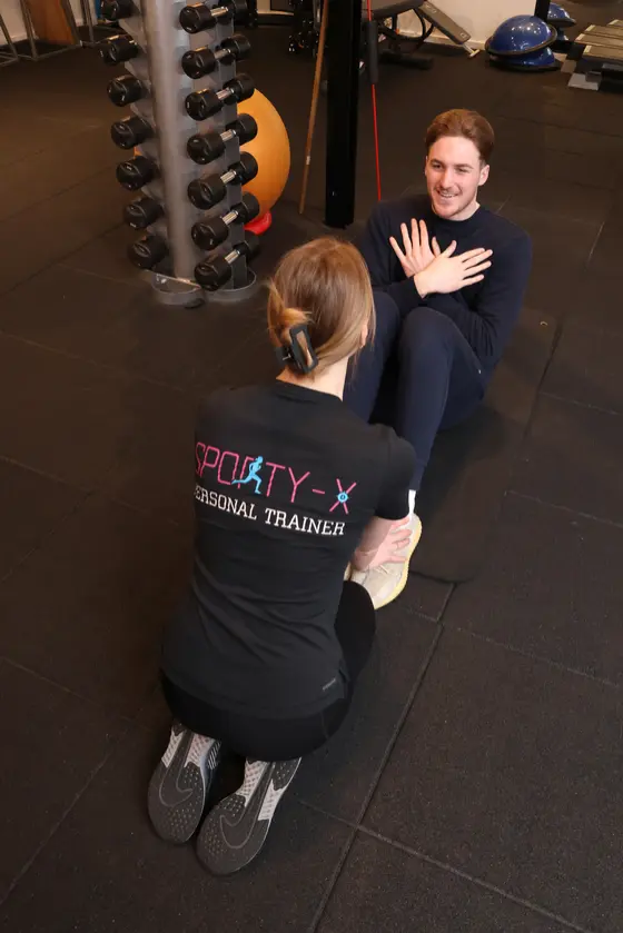 Een coach begeleidt een deelnemer op de trainingsvloer bij Sporty-x