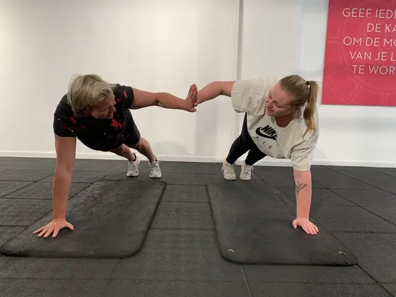 Twee deelnemers oefenen samen op de trainingsvloer bij Sporty-x