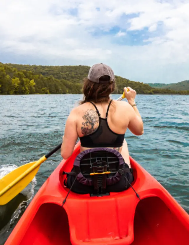 Member paddling a red kayak across a calm lake