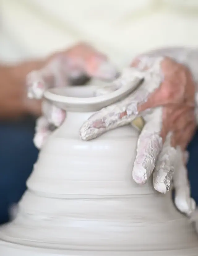 Hands shaping wet clay on a spinning pottery wheel