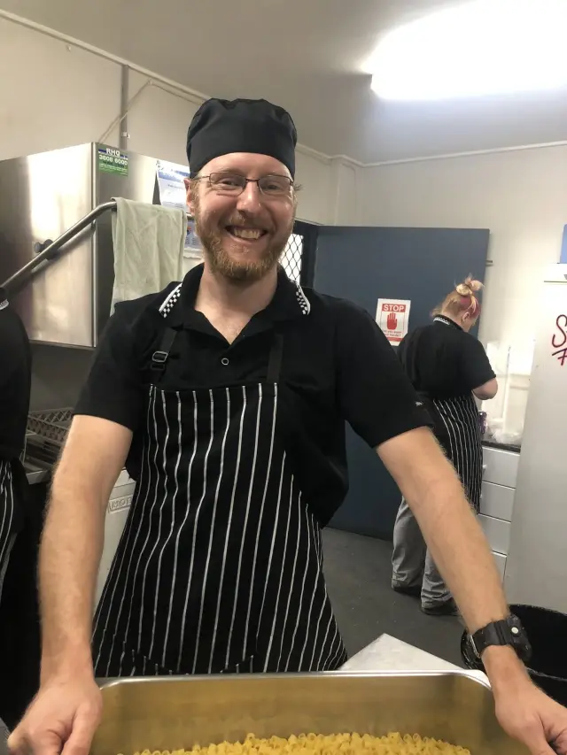 Smiling chef in an apron holding a tray in a commercial kitchen