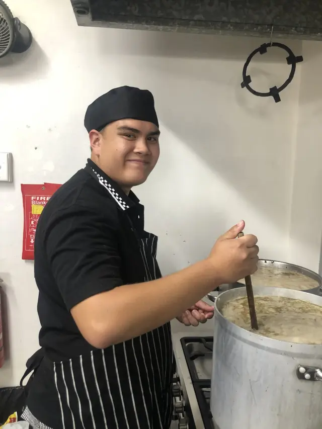 Young trainee cook stirring a large pot in the kitchen