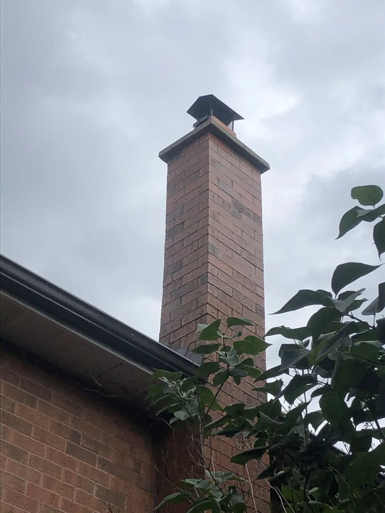 Rebuilt red brick chimney above a shingled roof